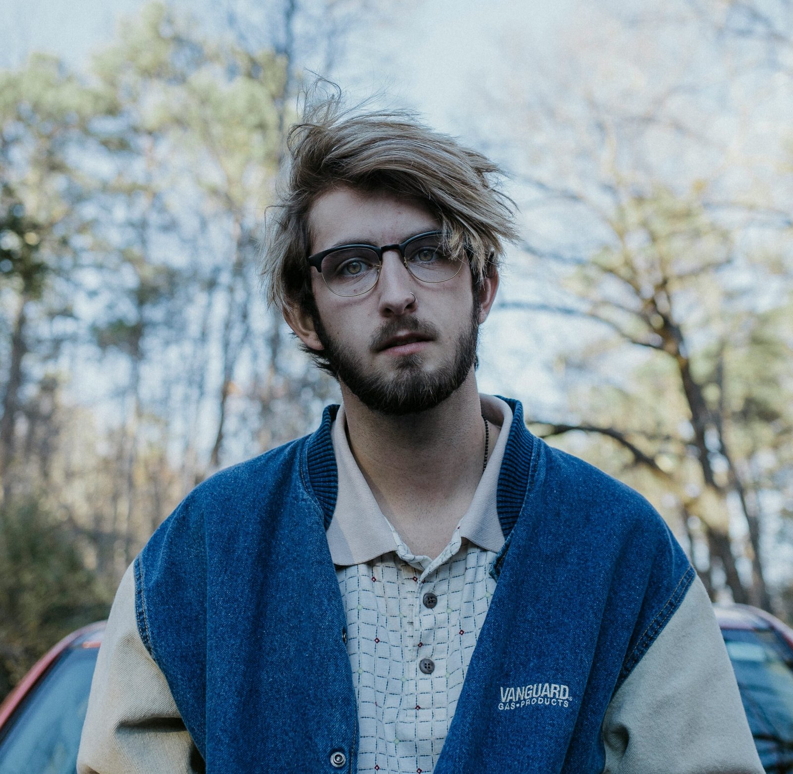 un hombre con barba y gafas delante de un coche